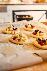 homemade buns with fruit and crumble on white baking paper ready for baking in the oven.