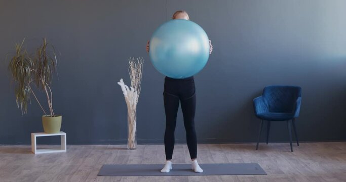 Young Sporty Woman is Exercising by Doing Squats with Fitball at Hands in Training Gym