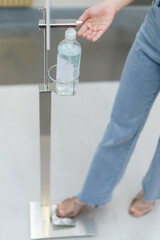 Woman using sanitiser dispenser foot pump.  Hand free alcohol hand gel dispenser. Stop Coronavirus...