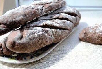 Composition in the bright rays of the daylight: homemade rye French mini baguettes (focus on bread in the center) and the texture of rough gray linen