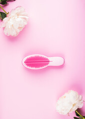 Pink hair brush for girls in frame of white peonies on pink background. Flat lay