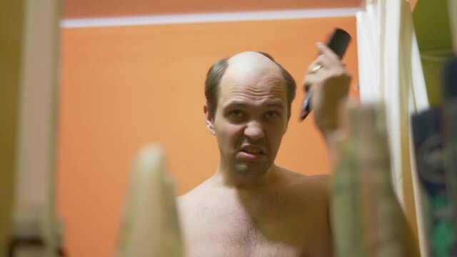 hair loss problem. balding man looks in the mirror, combes the remaining hair