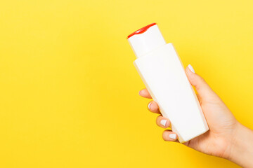 Female hand holding cosmetics bottle at yellow background with empty space for your design
