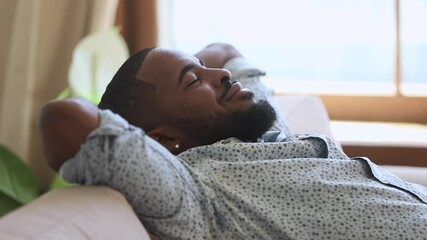 Calm relaxed lazy african american young man resting napping on sofa with eyes closed at home, happy healthy guy breathing fresh air lounge on couch hands behind head enjoy stress free peaceful day - Powered by Adobe