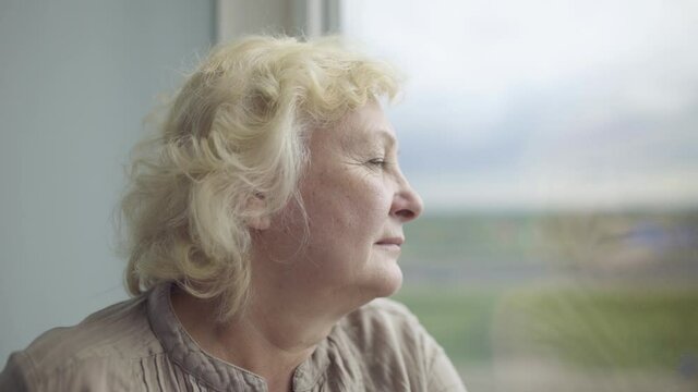 Thoughtful senior woman looking out the window, difficulties in old age, hope