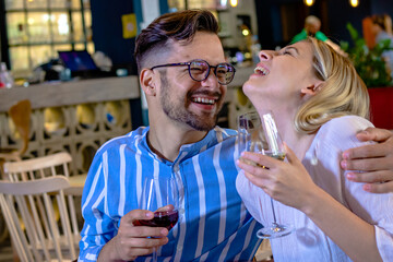 Happy young romantic couple laughing and toasting with wine glasses at dinner in a beautiful fancy restaurant.