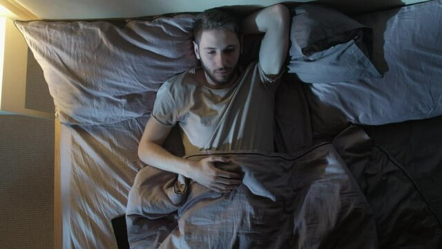Sleepless night. Insomnia problem. Tired man disturbed with anxiety trying to rest in bed.