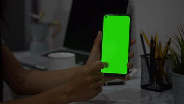 An over the shoulder shot of a young woman video chatting outside with green screen on her smart phone.