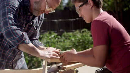 A father helps his son drive a screw in with a hand drill while working on a DIY carpentry project