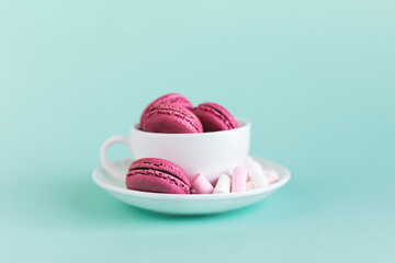 Tasty pink french macaroons with marshmallows in white cup on a turquoise background.