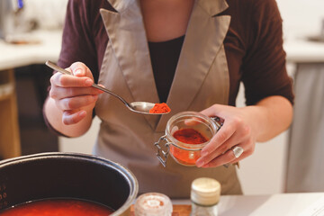 Female cook adds paprika spices while cooking tomato soup.Close-up view on spoon with red pepper.