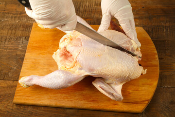 Woman cuts chicken carcass in half with a knife on a wooden board. © finist_4