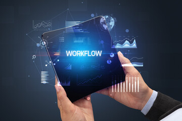 Businessman holding a foldable smartphone with WORKFLOW inscription, successful business concept