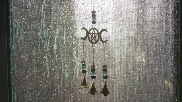 Static shot of a pentagram chime hanging in a screen window wet with rain droplets