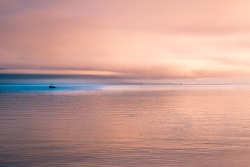 A sunset view of the coast of Alaska with a small fishing boat in the blue water
 


