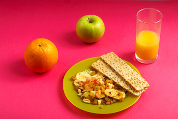 diet bread and granola on a plate, orange, apple and a glass of juice on a pink background.