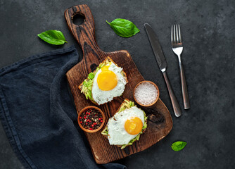 Toasts with avocado and fried eggs on a cutting board on a stone background
