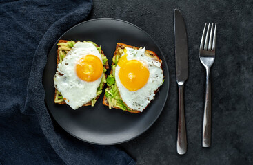 Toasts with avocado and fried eggs on a cutting board on a stone background