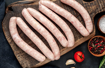 Raw sausages with spices on a cutting board on a stone background
