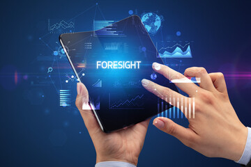 Businessman holding a foldable smartphone with FORESIGHT inscription, successful business concept
