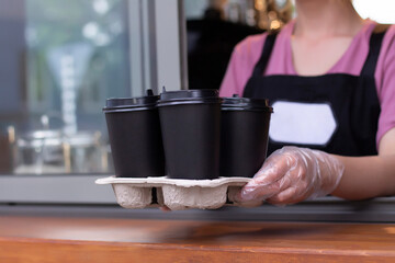 Takeaway coffee. Barista in an apron holds hot coffee in a paper cup in his hands. Coffee pick up at cafe shop.