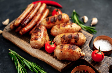 Different grilled sausages with spices and
rosemary, served on a cutting board on a stone background