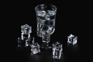 Glass decanter and stemmed glass, ice cubes, on a black background. The texture of the glass.