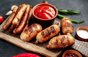 Different grilled sausages with spices and
rosemary, served on a cutting board on a stone background