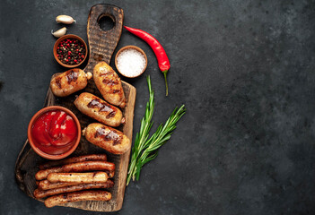 Different grilled sausages with spices and
rosemary, served on a cutting board on a stone background with copy space for your text