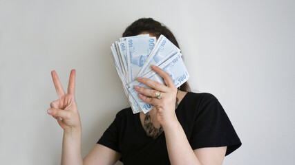Portrait of a happy excited cheerful young woman holding bunch of money banknotes and celebrating isolated on white background. Woman showing victory sign / ok sign / great or good sign