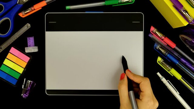 Female hand drawing on digital tablet from top view closeup 4K. Desktop view of creative business woman working. Young illustrator making sketch using pen.