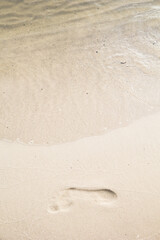 Footprint in the sand with pure water and little waves. Vertical view. Summer vacation near water. Travel conception