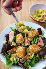 Fancy salad with goat cheese balls, figs and mango over a wooden table. 