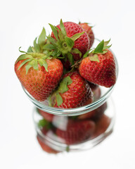 A clear glass bowl of red strawberries with reflection on a mirror.  White background.