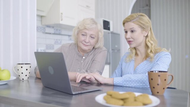 Young female and mother looking at laptop screen, discussing photos, booking app