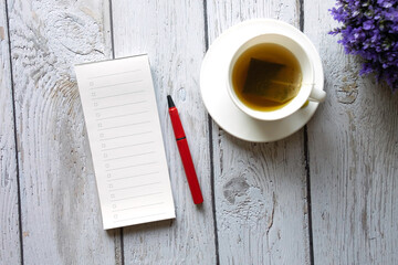 Top view blank open notebook with red pen on wooden table.A cup of hot tea with saucer and purple plant on table..