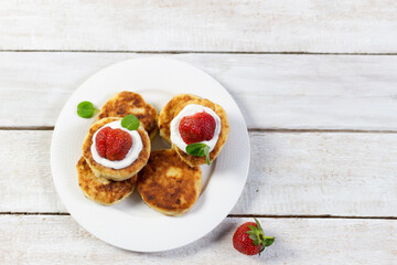 cheesecakes with sour cream, strawberry, mint leaf on plate  on white wooden background