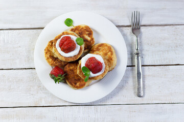 cheesecakes with sour cream, strawberry, mint leaf on plate with fork on white wooden background