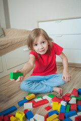 Little girl in a red T-shirt in a nursery wants to throw a die, is angry. Vertical photo