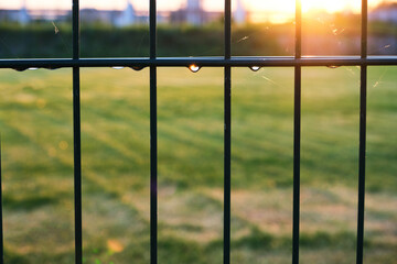 Football field fence in water drops after irrigation of the field with water at sunset.