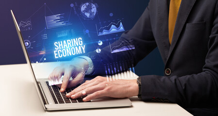 Businessman working on laptop with SHARING ECONOMY inscription, new business concept