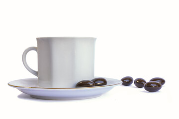 White porcelain cup on plate and chocolate candies around, isolated on white background. Tea break concept, snack, hot beverage. Luxury porcelain utensils.