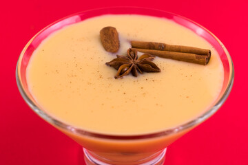 Glass of christmas eggnog drink with bourbon on a red background.