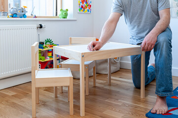 Fototapeta na wymiar A parent assembling flom flat pack a set of two small chairs with desk in childs bedroom.