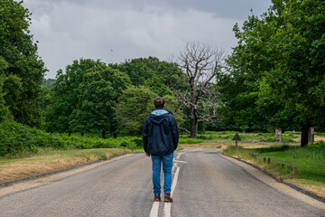 Photo of a young and attractive man walking in the middle of a road in the nature in RIchmon Park, London