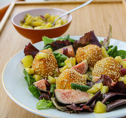 Fancy salad with goat cheese balls, figs and mango over a wooden table. 