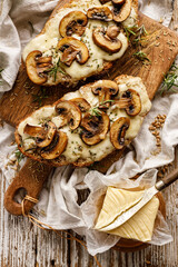 Toasted sandwich from traditional sourdough bread with cheese and brown mushrooms seasoned with rosemary herb on a wooden board, top view