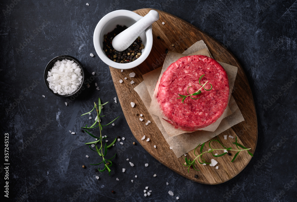 Wall mural Raw ground beef meat burger steak cutlets with salt and rosemary on dark background. Top view.