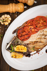 Grilled fish on a white plate with tomatoes, micro greens, lemon and garlic.
