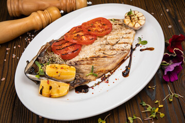 Grilled fish on a white plate with tomatoes, micro greens, lemon and garlic.
